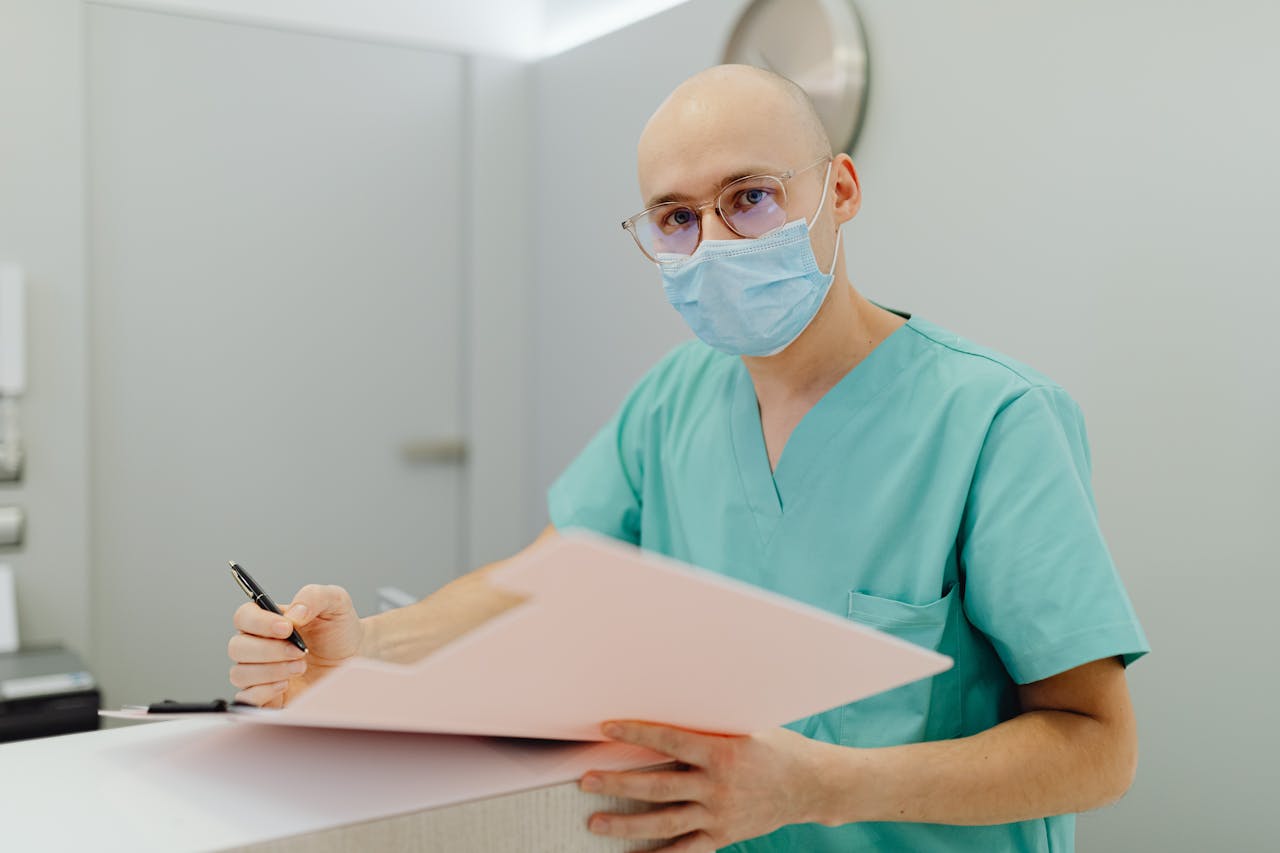 Medical professional in scrubs with mask, focusing on patient care documentation.